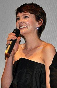 A woman stands and smiles, holding a microphone