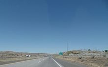 A divided highway crossing shrublands and approaching a sign