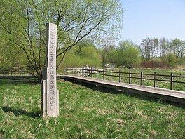 A wooden signpost with "Tiefwerder Wiesen" carved into it indicating the start of a boardwalk through a grassy area.