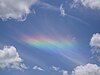 Clouds against a blue sky with a multicolored rainbow-like shine