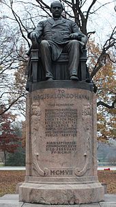 A statue of a middle-aged gentleman sitting in an impressive chair atop a column about five feet tall. "To Marcus Alonzo Hanna" it is marked, with a short message detailing his "efforts for peace between capital and labor" given beneath. A year is finally given in Roman numerals near the base: "MCMVII", or 1907.