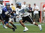 A lacrosse player advancing, pursued by an opponent