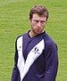 An Australian cricketer wearing a purple-white shirt and looking to his left.