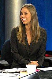 A woman in a back suit sitting in front of a desk with scattered papers