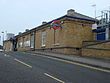 A brown-bricked building with a rectangular, dark blue sign reading "PINNER" in front of a road all under a cloudless, light blue sky