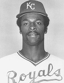 A man in a light baseball jersey and dark cap