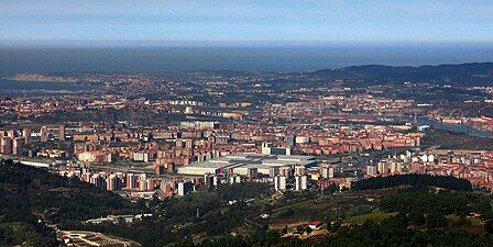 Panoramic view of Barakaldo showing numerous small buildings covering a wide area with green hills in the foreground and background