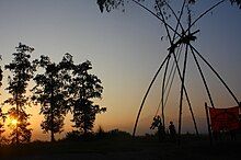 A picture of a swing made from four bamboo plants, during dawn time