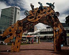 A wooden carved entrance arch in the middle of the photo. The arch is triangular with two posts and is quite large. The carvings are a mixture of shapes and some stick out of the top.