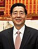 a smiling, clearly aged man with wavy haircut, wearing glasses, a white shirt, a suit and a light red tie