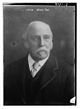 A photographic portrait of a man, showing his head and shoulders. He has a moustache and grey, balding hair. He wears a jacket, a shirt with a turn-down collar and tie.