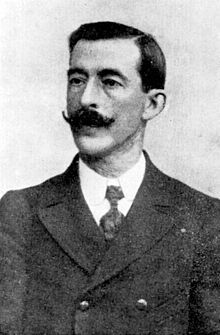 Portrait photograph of Ricardo Mella, wearing a suit and a well-groomed moustache