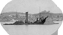 Armored steamboat in front of bluffs with buildings