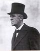 a photograph of an older man wearing a top-hat, an overcoat, a shirt with a turned down collar and a bow-tie.