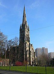 A stone church seen from a slight angle at the southwest, with a tower and tall spire on the left and the body of the church extending to the right