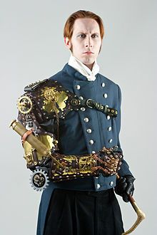 G. D. Falksen in steampunk attire, including a mechanical arm wearable sculpture by Thomas Willeford, utilizing a complex clockwork series of gears