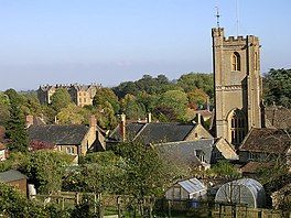 View of the roofs of houses with a prominent square church tower, interspersed with trees.