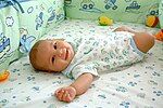 A smiling baby lying in a soft cot