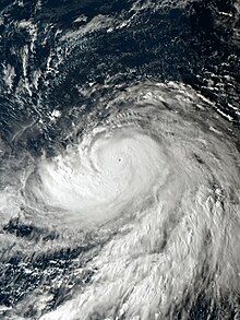 A photograph of an extremely powerful typhoon over the western Pacific Ocean. It has a pinhole eye surrounded by intense convection; the cloud tops of thunderstorms are billowing near the eye. Gravity waves radiate outward from the eye; this is a characteristic of many powerful tropical cyclones. Large, well-defined rainbands spiral out well to the south of the center of the typhoon. Thin, roughly parallel streaks of high, wispy clouds are emanating to the northeast and southwest of the typhoon, indicating that it has healthy outflow, which is something that helps tropical cyclones to intensify.