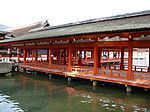 A wooden roofed corridor on stilts over water with red beams and red handrails.