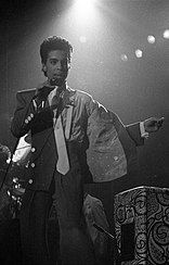 A black-haired man in a suit and tie performing onstage