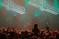 Zoot Woman live in concert, performing amidst fog and red lighting in front of a large audience