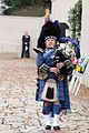 Piper in full Highland Dress with Feather Bonnet in place of Glengarry and blue-grey Doublet with gold braid in place of black with silver braid