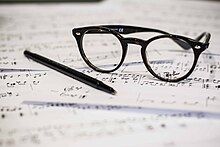 A pair of eye glasses and an ink pen rest on top of some sheet music