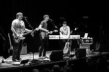 Several men performing onstage playing instruments and singing into a microphone