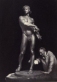 A black and white photograph of a sculpture of a man, with the sculptor behind it