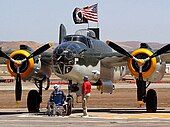 Closeup of bomber on tarmac with two older men, one in a wheelchair looking on