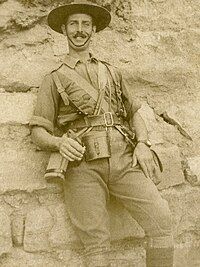 An informal, sepia portrait of a man in military uniform. He is leaning against what appears to be a wall.