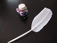 Picture of a quill and a small bottle of ink on a table.