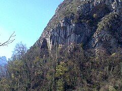 Rocky walls ending in a cave, practically overgrown with vegetation.