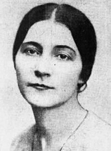 A white woman with dark hair parted center and drawn back low on the nape.