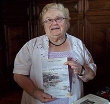 Lucette Desvignes, a white woman in her 80s, holding one of her books