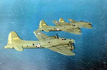 Three olive green four-engined propeller aircraft fly over the ocean.