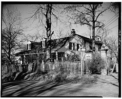 Exterior view of Casa Alvarez, showing several trees, white clapboard siding, front porch, wooden fence, and front two dormer windows