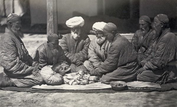 Men seated on the ground near a small boy who is being circumcised, Central Asia