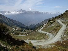 Photo of a mountain pass in the foreground, the steep road leading up to it and mountains on the horizon.