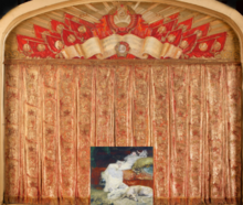 A woman and a Borzoi (dog) sit behind the Bolshoi Theater's CCCP iconographic laden curtain.