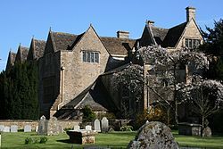 Old mansion house with triangular roofs. In the foreground is a garden with gravestones.