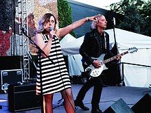 Corin Tucker pointing and holding a microphone beside Peter Buck playing guitar