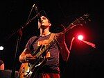 Sufjan Stevens performing on stage during a tour for Illinois. Stevens and his band the Illinoisemakers wore outfits modeled after those of the cheerleaders of the University of Illinois.