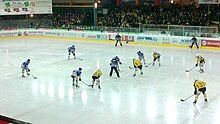 Ice hockey players on a field holding their sticks, some wearing blue and others wearing yellow