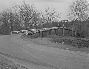 A monochromatic image of a truss bridge held up by stone pillars