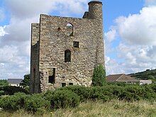 Ruined and overgrown stone building with a tall stone chimney