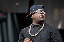 Big Boi dressed in black, with a gold chain and baseball cap turned sideways