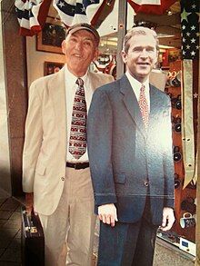 Sherwood Ross, briefcase in hand, poses next to a cardboard cutout of Pres. George W. Bush. The photo was taken around the corner from the National Press Club in Washington, DC.