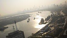 A curving river at dusk lit with diffuse light. Ships and docks can be seen on the river